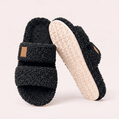 Fuzzy two-strap slides in Black, one flat and one tilted to show the wavy cream sole