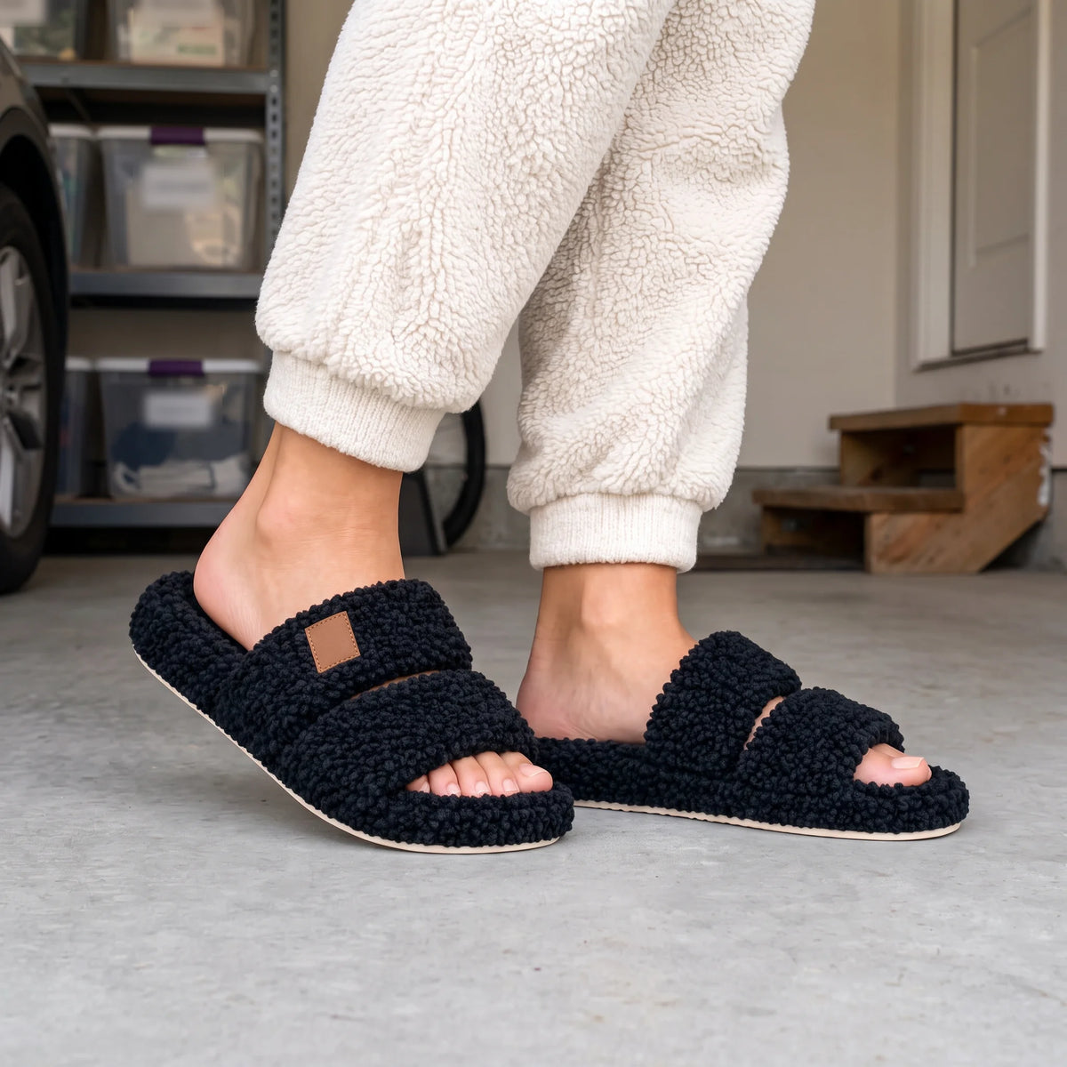 Black fuzzy two-strap slides worn on a concrete garage floor