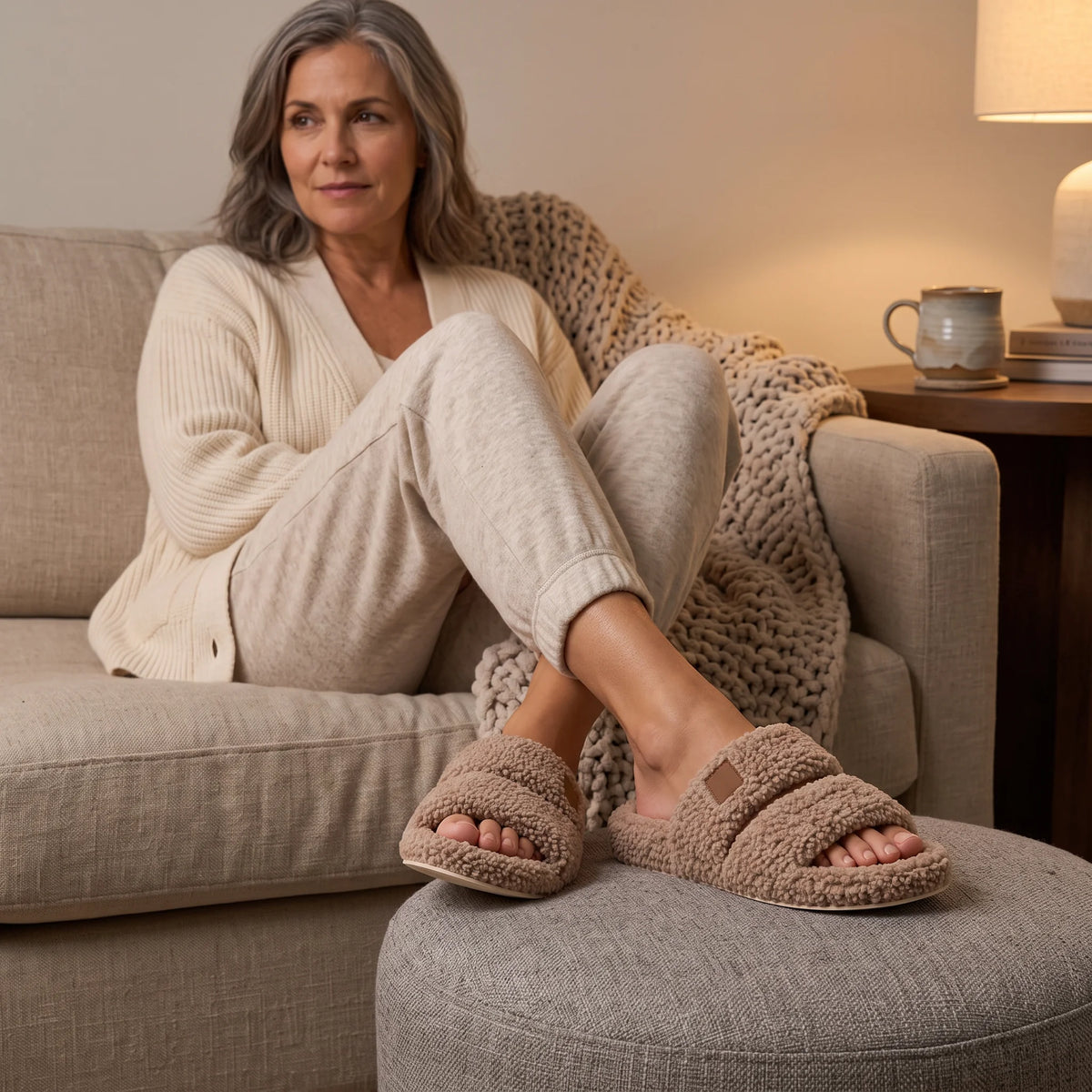 Woman relaxing on the sofa with her feet crossed on an ottoman, wearing fuzzy two-strap slides