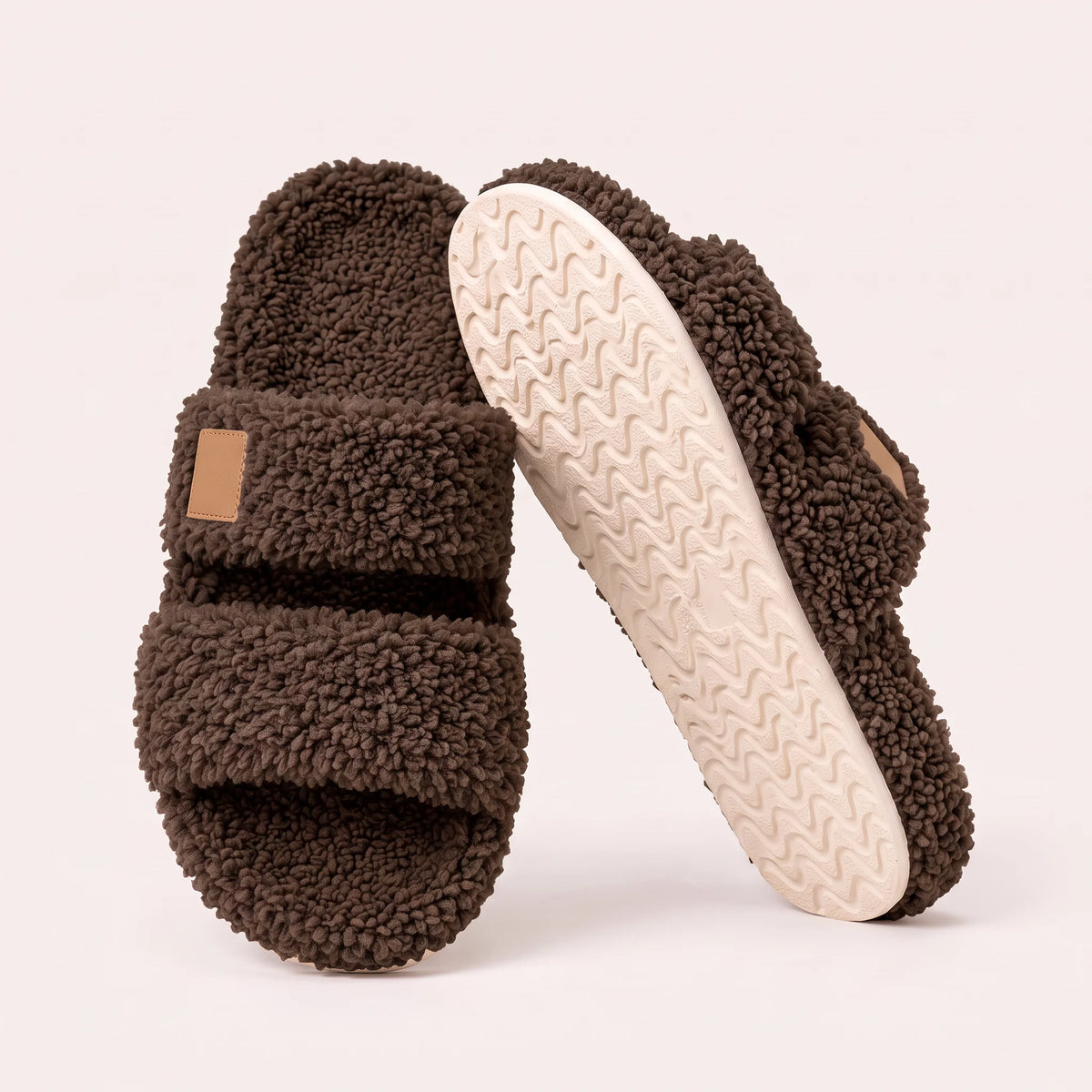 Fuzzy two-strap slides in Chocolate, one flat and one tilted to show the wavy cream sole