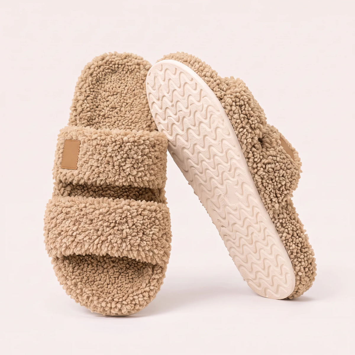 Fuzzy two-strap slides in Sand, one flat and one tilted to show the wavy cream sole