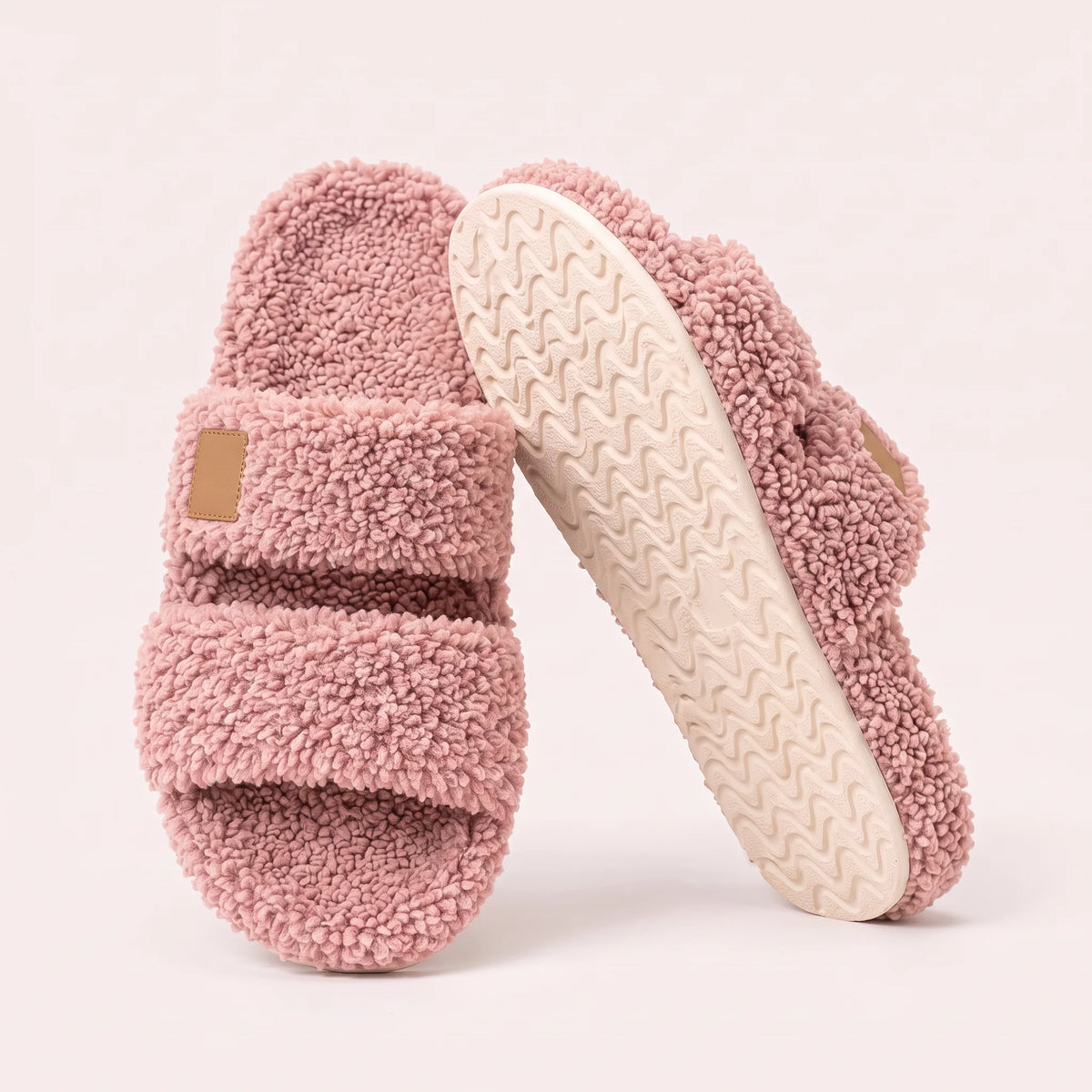 Fuzzy two-strap slides in Blush Pink, one flat and one tilted to show the wavy cream sole